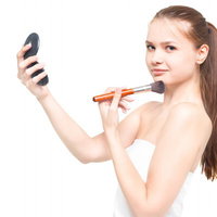 コンパクトミラーを持ちながらチークブラシを頬に当てるロシア人女性の写真