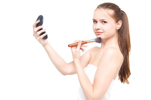 コンパクトミラーを持ちながらチークブラシを頬に当てるロシア人女性