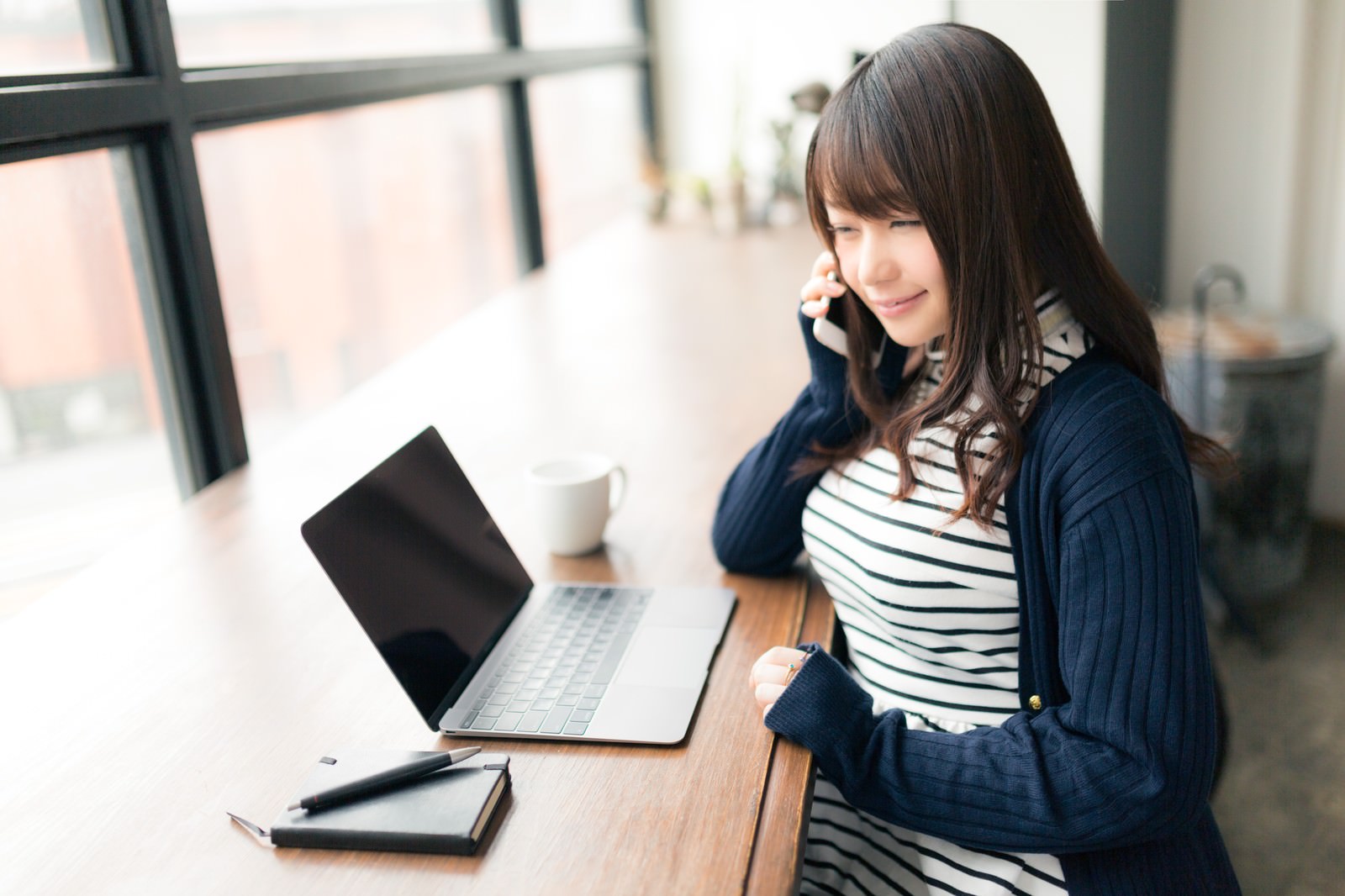 デスクでパソコンと電話を同時に使う笑顔の女性