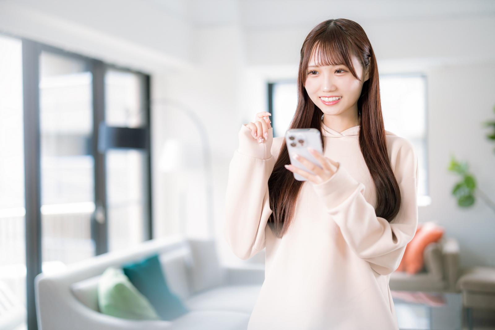 スマートフォンで部屋探しをする笑顔の若い女性［モデル：あき］