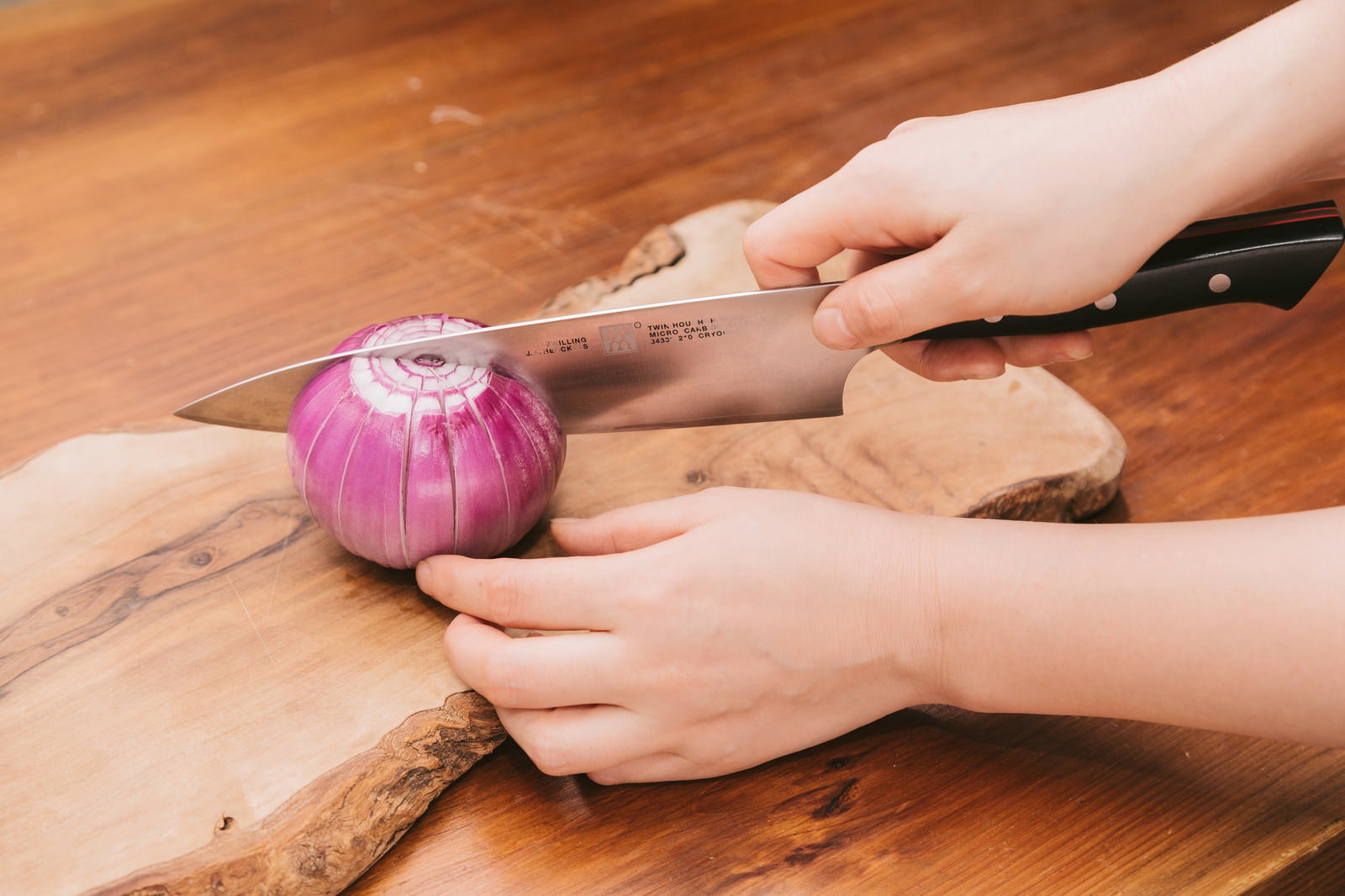 まな板で赤玉ねぎを包丁でカットする手元
