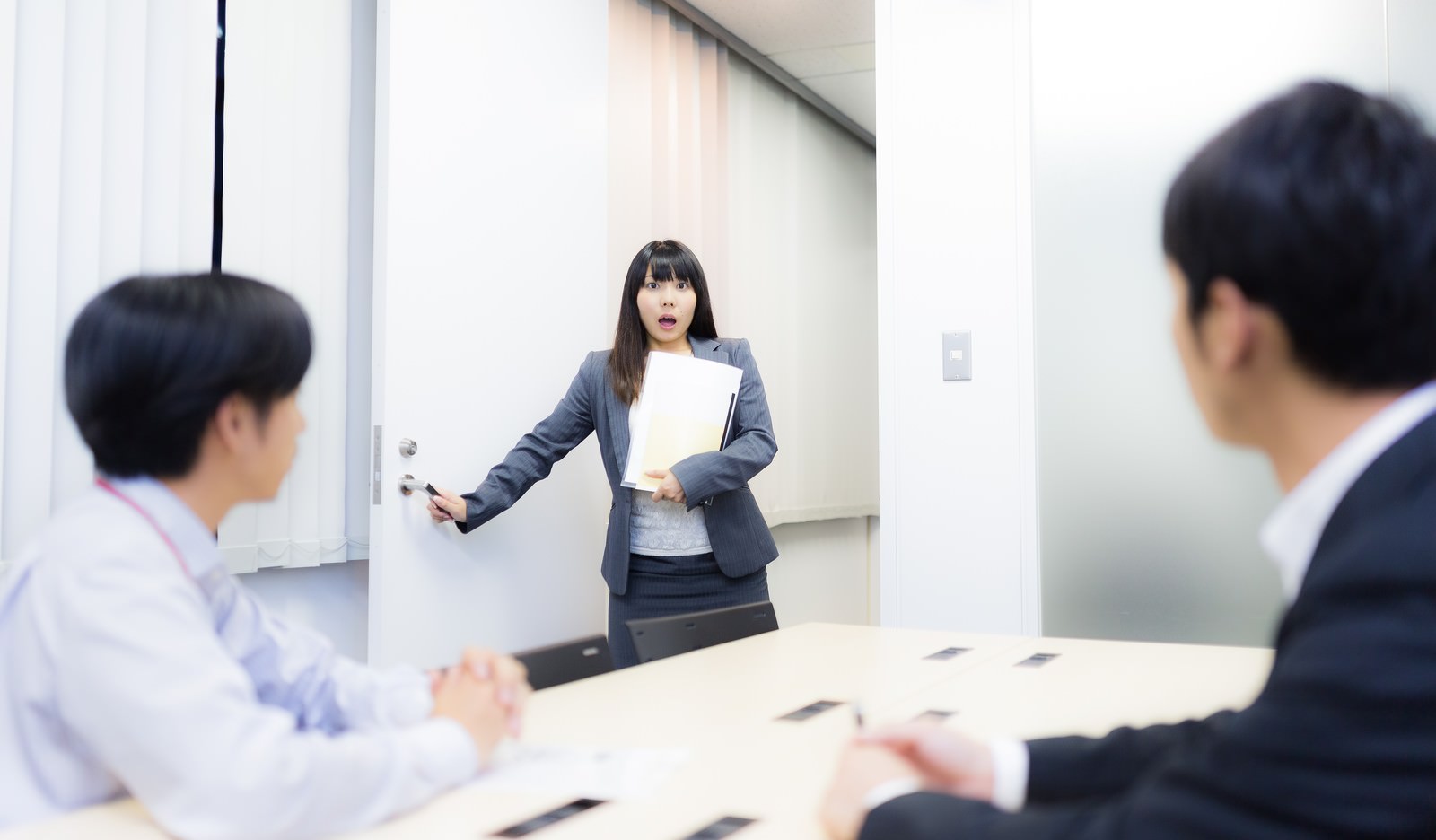 書類を持って会議室のドアを開けた瞬間に部屋を間違えたと気づき驚く女性ビジネスパーソン［モデル：Lala］