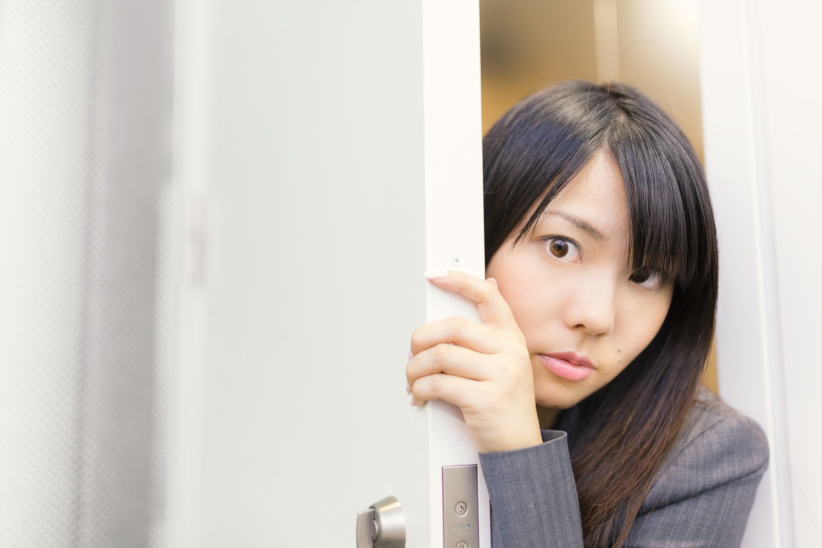 ドアの隙間から覗くスーツ姿の女性社員［モデル：Lala］