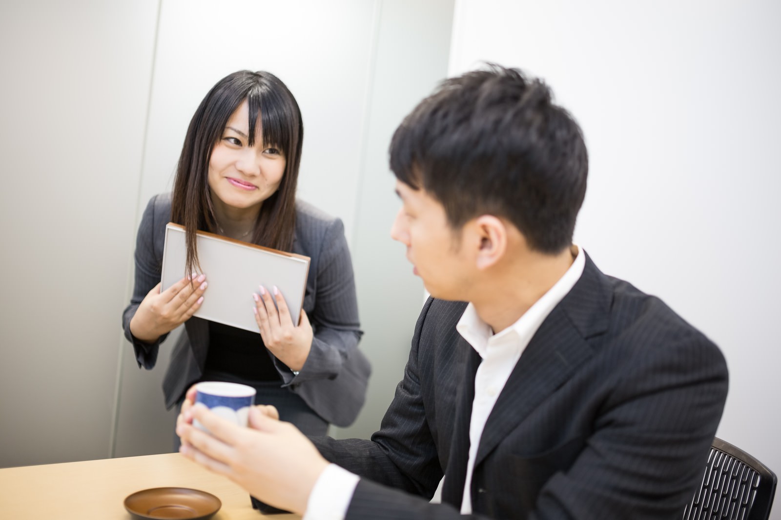 紙コップを持つ男性に白い紙を見せるジャケットの女性［モデル：大川竜弥 Lala］