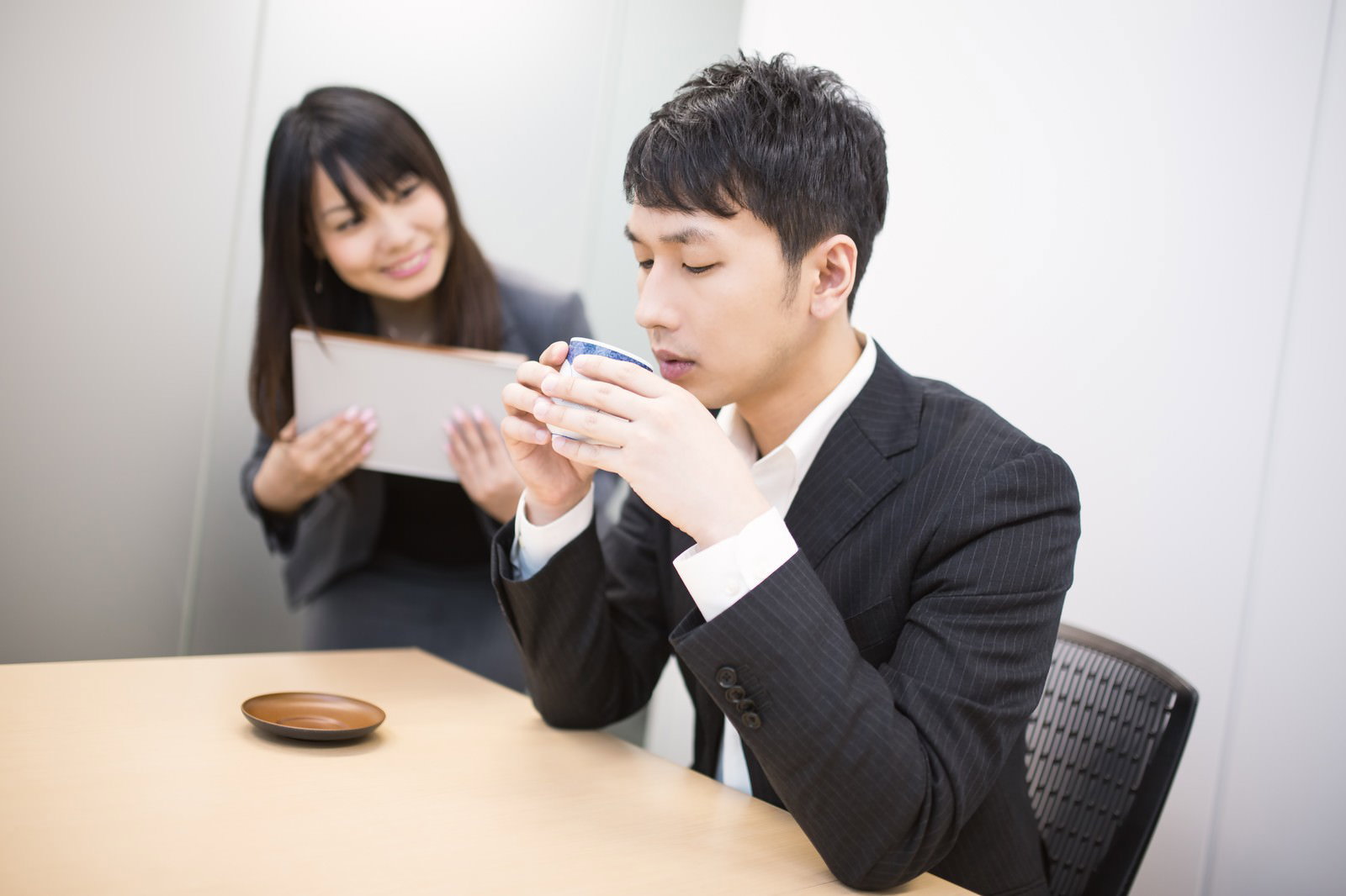 会議室でお茶をすするスーツ姿の男性［モデル：大川竜弥 Lala］