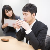 女性社員に見つめられながらお茶をすするビジネスマンの写真