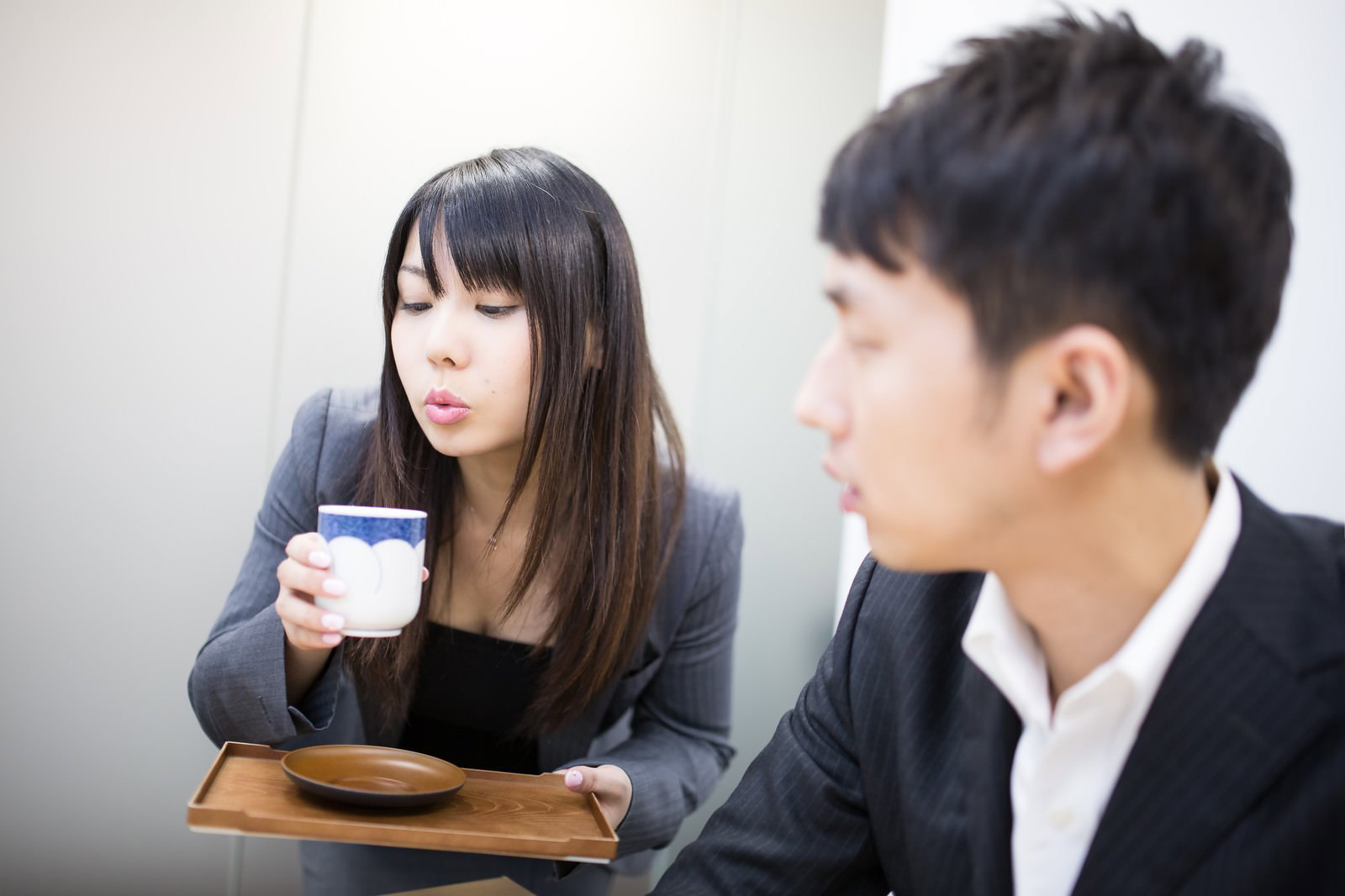 湯のみをフーフーしながら目配せするスーツ姿の女性［モデル：大川竜弥 Lala］