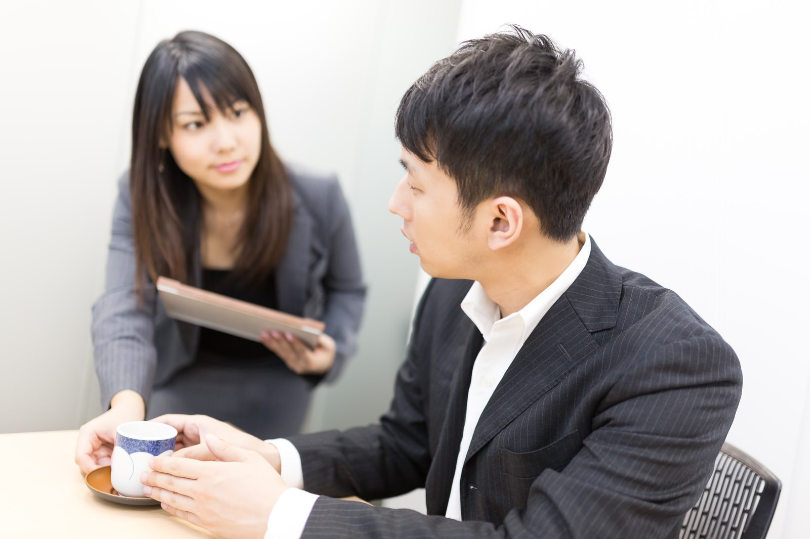 カップを手に持つ男性とタブレットを持つ女性の打ち合わせ［モデル：大川竜弥 Lala］