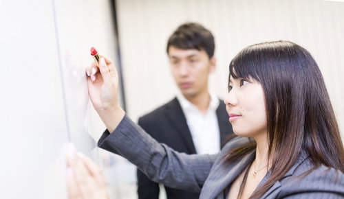 ホワイトボードに書き込む女性社員と見守る男性