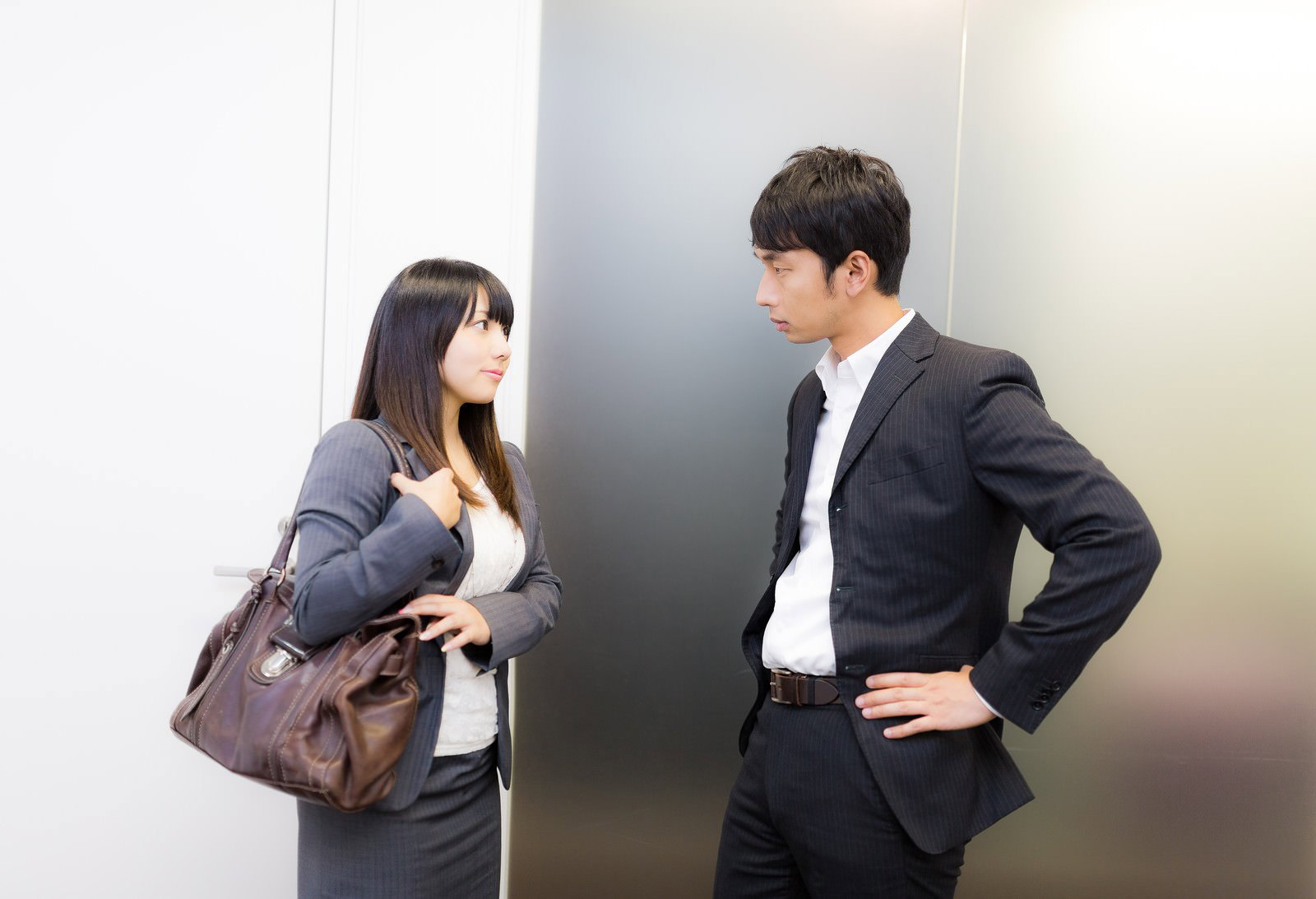 エレベーター前で上司に報告する女性社員［モデル：大川竜弥 Lala］