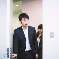 会議室のドアを開けて入室するスーツ姿の男女の写真
