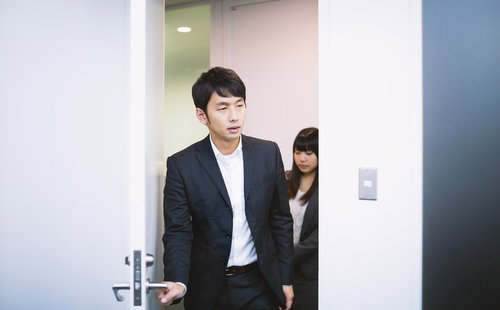 会議室のドアを開けて入室するスーツ姿の男女