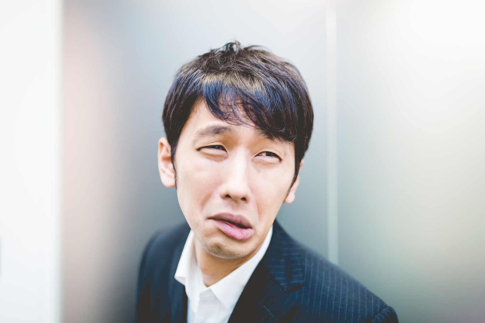 紺色のスーツを着た男性が目を細め口を左右に引いて顔をゆがめている［モデル：大川竜弥］