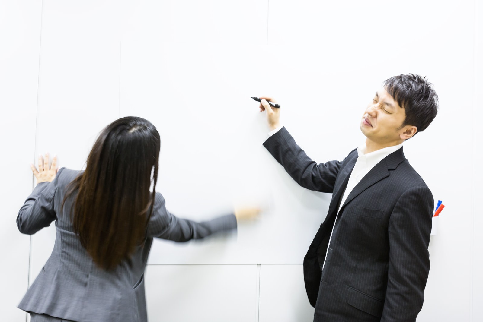 ホワイトボード前でやりとりする男女社員［モデル：大川竜弥 Lala］