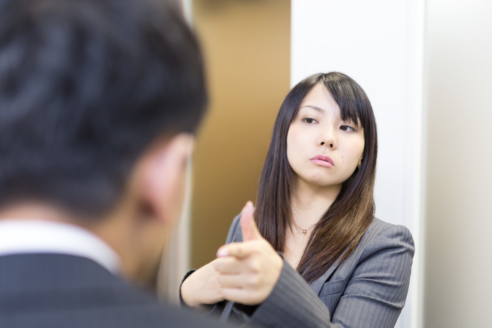 グレースーツの女性が男性に指を指しながら叱責している会議室［モデル：大川竜弥 Lala］
