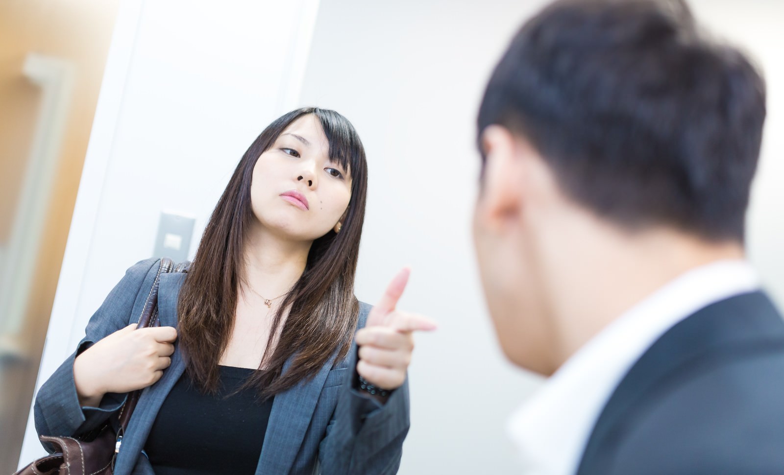 紺のスーツを着た女性が、背を向けた男性に指を向けて厳しく言葉を投げかけている［モデル：大川竜弥 Lala］