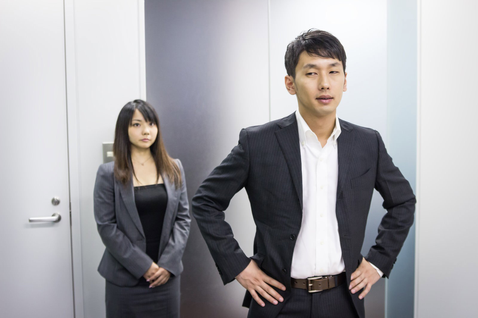 オフィスで身を乗り出して話す黒いスーツの男性上司と聞き手の女性社員［モデル：大川竜弥 Lala］