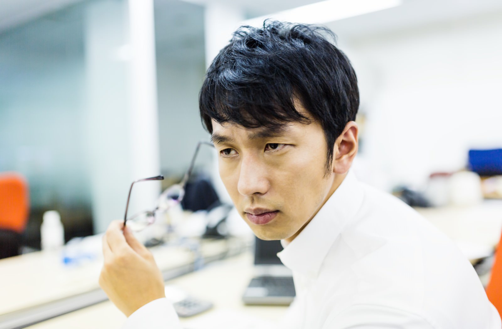 オフィスデスク前でメガネを外し決めポーズをする白シャツの男性会社員［モデル：大川竜弥］