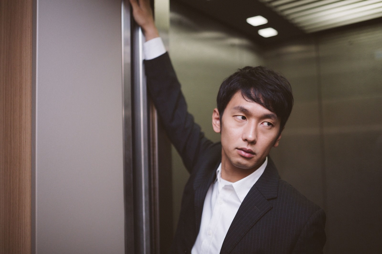 エレベーター内でドアを開いたまま保つスーツ姿の男性が、相手の乗降を促している［モデル：大川竜弥］