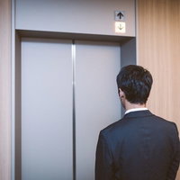 エレベーターを待つスーツ姿の男性、昇降表示を見つめるの写真