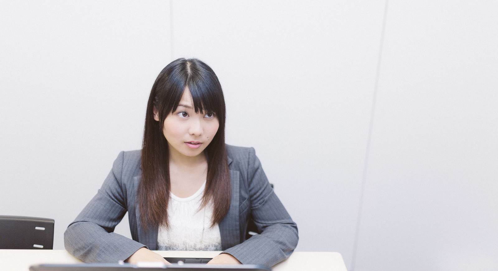 会議テーブルで両腕を置き、前方を見つめながら指示を出すグレースーツの女性社員［モデル：Lala］
