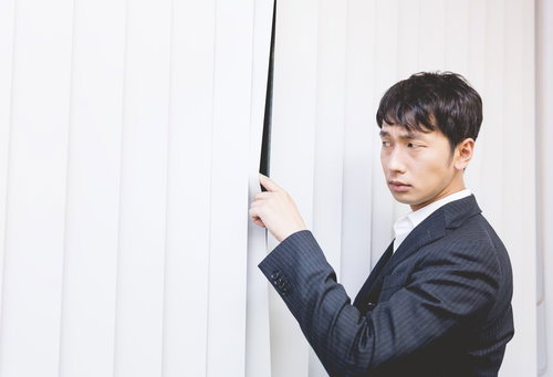 ブラインド越しに外の様子を気にする会社員男性