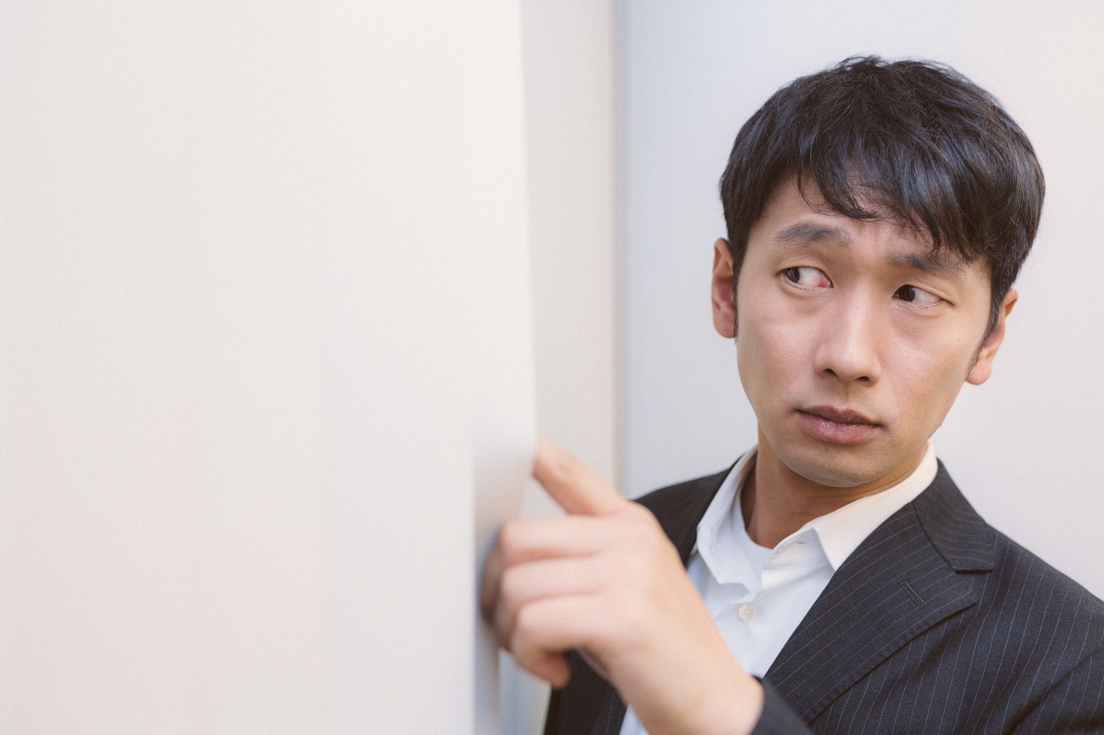 スーツ姿の男性がブラインドの隙間に手をかけ、外を見下ろしている［モデル：大川竜弥］