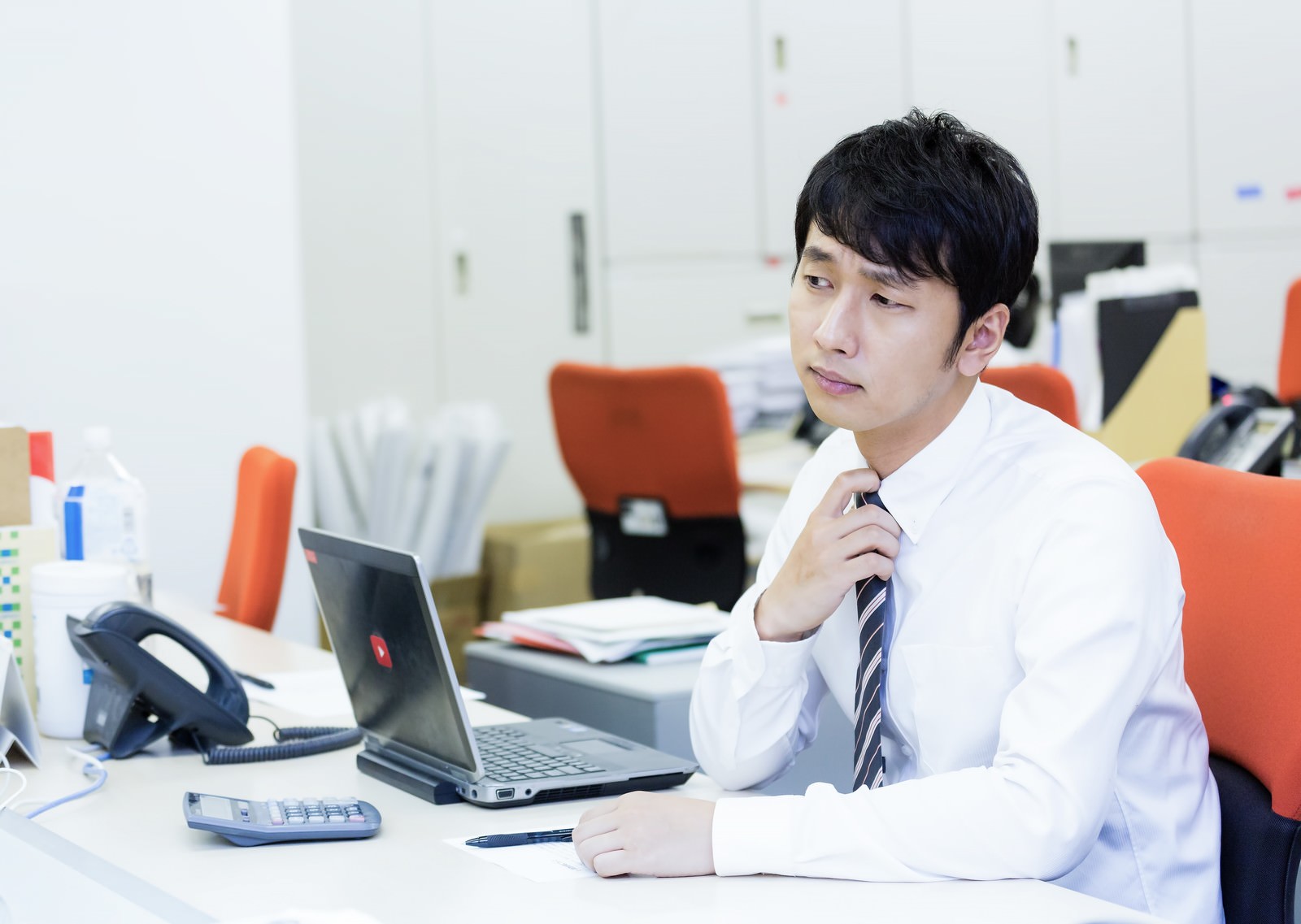 オフィスのデスクでネクタイを緩める白シャツ姿の男性会社員［モデル：大川竜弥］