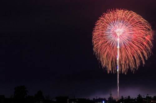 夜空に咲く遠くの打ち上げ花火が放射状に広がる夏祭りの風景