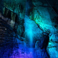 青い光にライトアップされた滝観洞の滝と岩壁の写真