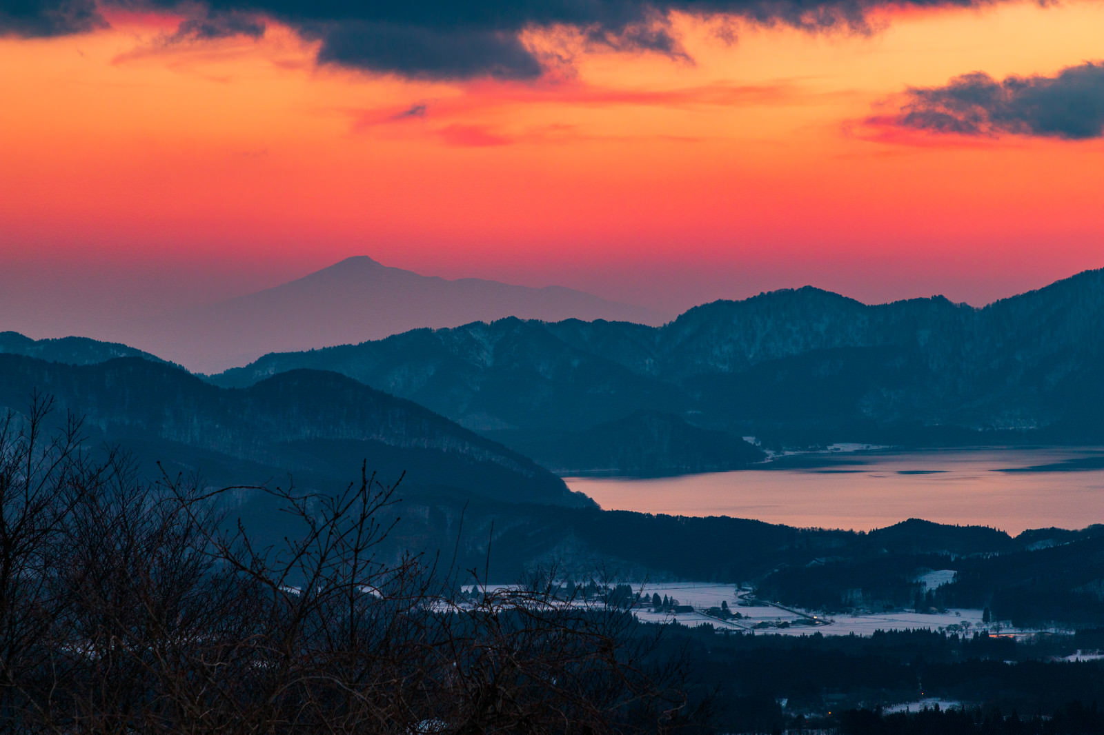 オレンジからピンク色に染まる夕焼け空の下、田沢湖と鳥海山が重なるシルエット