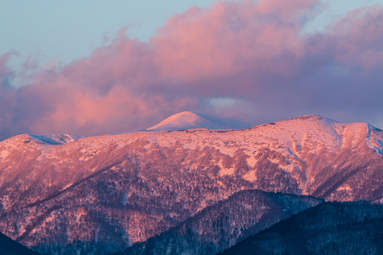 夕焼けに染まる空の下、雪が残る秋田駒ヶ岳の山々
