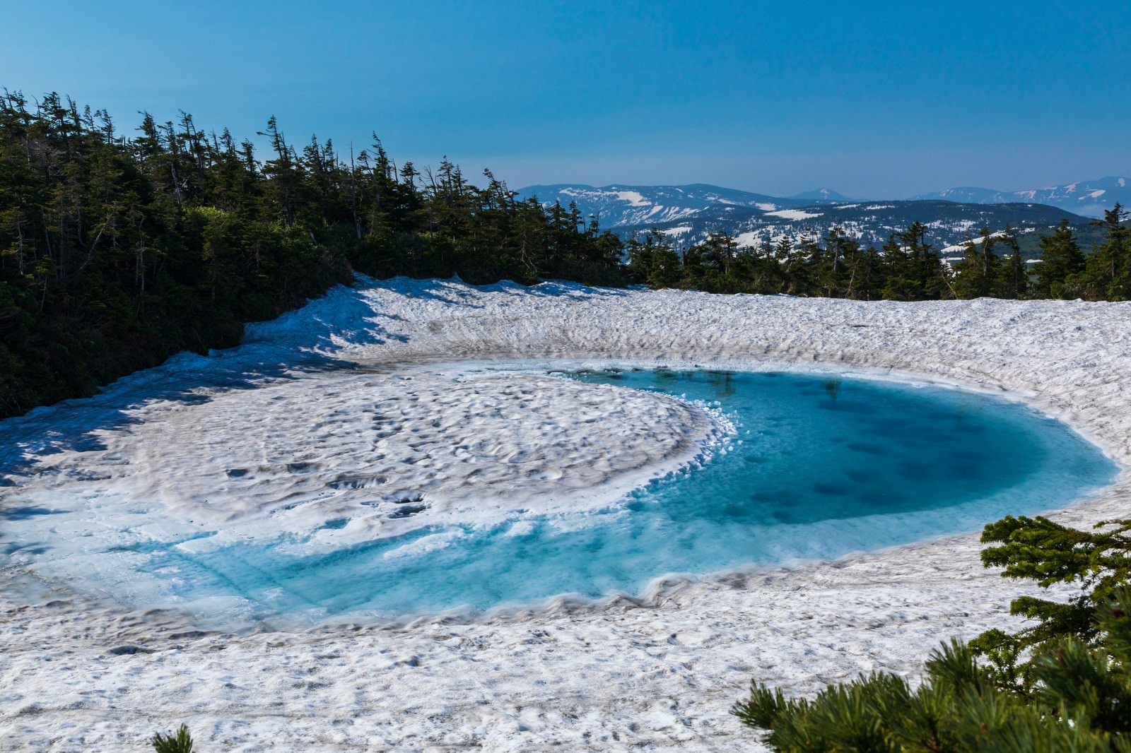 残雪の中に青い水面が広がる八幡平ドラゴンアイを上から見た風景