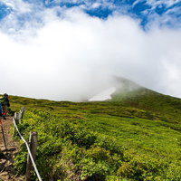 沸き立つ雲の中へと進む登山者（秋田駒ヶ岳の登山道）の写真