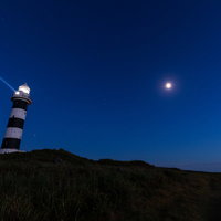 入道埼灯台からの夜空への照射と灯台建物の夜景の写真