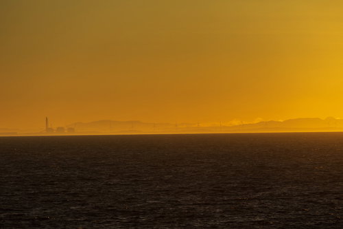 朝靄の中に浮かびあがる風車群と朝焼けの海