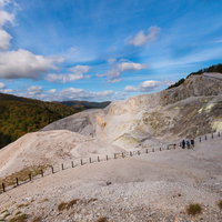 広大な川原毛地獄の白い岩肌を歩く登山者たちの写真