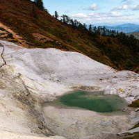 川原毛地獄の白い岩肌とエメラルドグリーンの池の写真