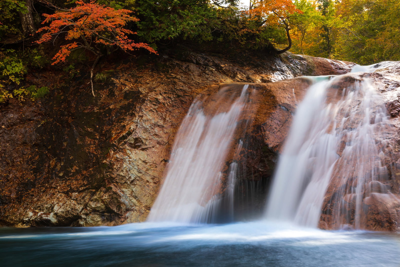 秋の山で色づいた紅葉と岩肌を流れる滝の風景
