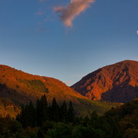 夕暮れに染まる紅葉した山と空に浮かぶ月の秋風景の写真