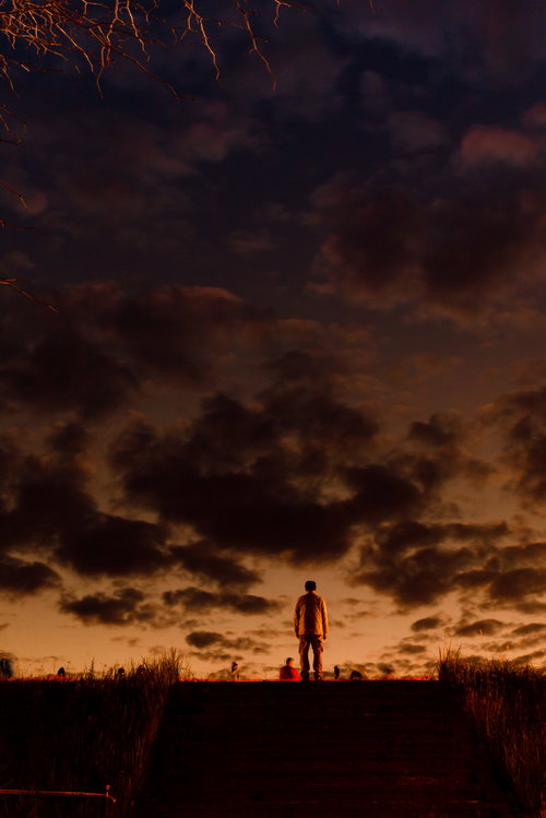 階段のある土手の上から夕焼けを眺める男性のシルエット