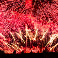 花火の光跡で赤く染まる大曲の秋の夜空（秋田県大仙市）の写真