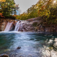 紅葉の間から差す日と赤滝～秋田の渓谷の写真