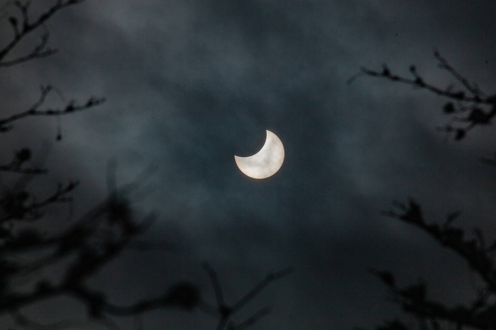 薄雲に覆われた空で三日月状に欠けた太陽が見える日食現象