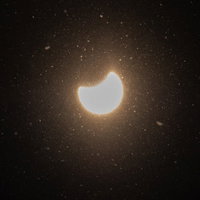粉雪舞う日食現象：暗い空に欠けた太陽と細かな雪片の写真