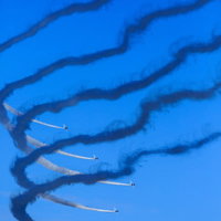 青空を背景に急カーブするブルーインパルスの編隊飛行と白い航跡の写真