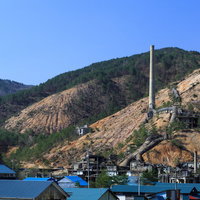 地すべりが起きそうな山肌に立つ鉱山跡の煙突の写真