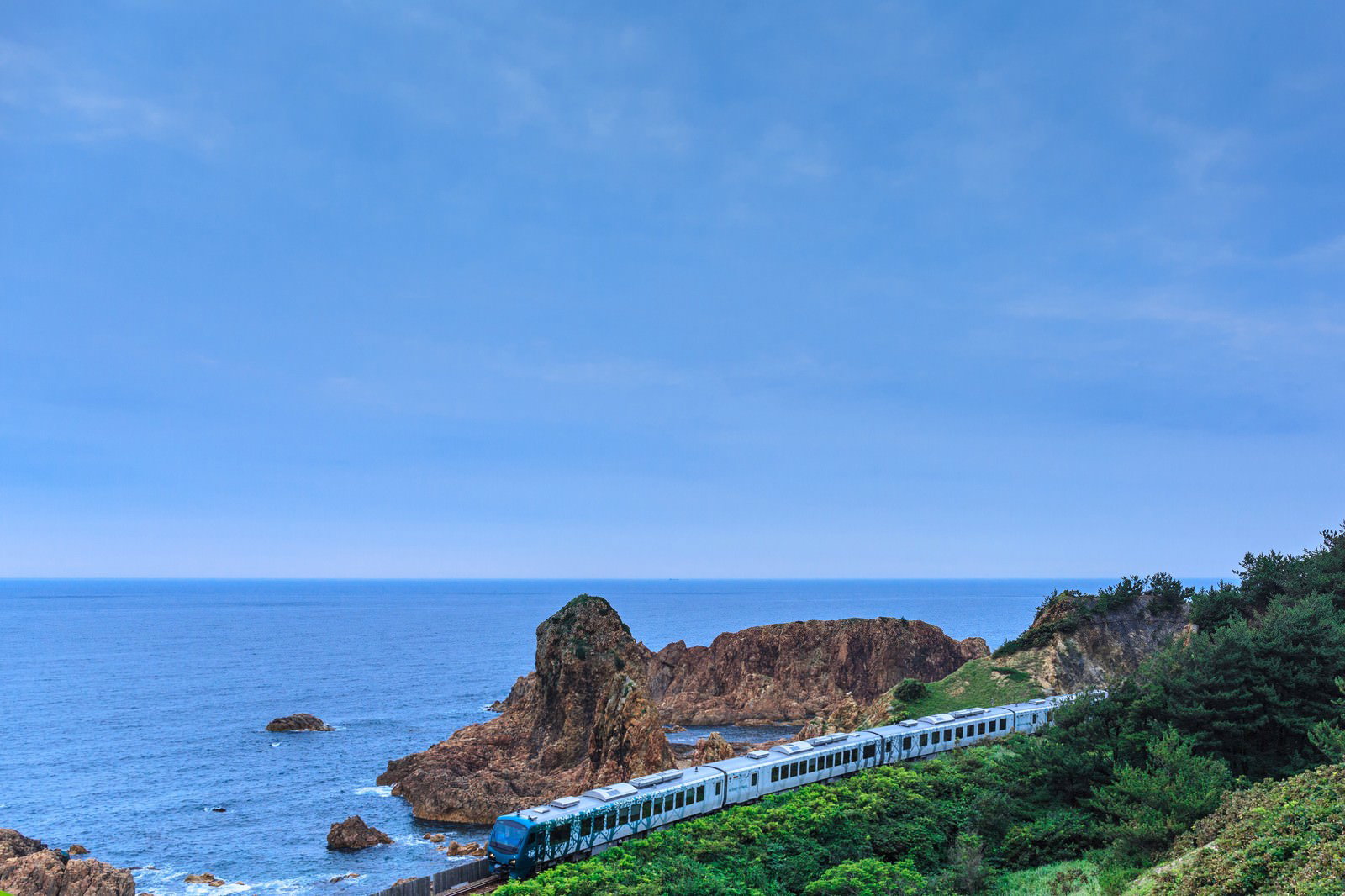 日本海の岩礁沿いを走る青と白の列車