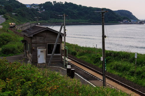 海沿いのローカル線の無人駅の線路と駅舎の風景