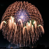 夜空に弾ける打ち上げ花火のオレンジと白の光跡の写真